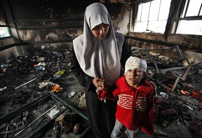 Palestinská ena drí za ruku svého syna uprosted znieného domu